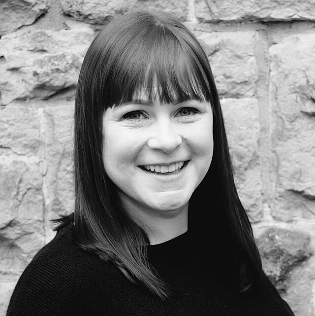 A woman is smiling in front of a stone wall.